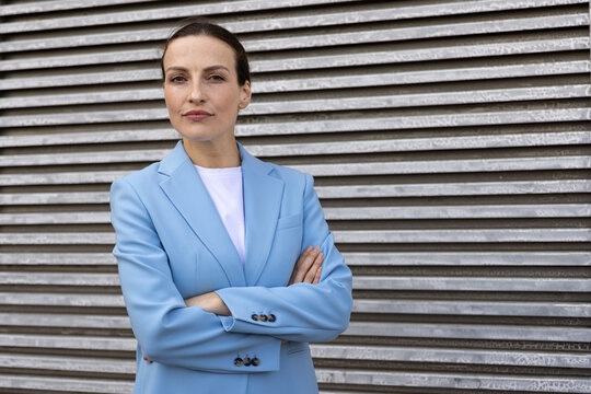 Female entrepreneur wearing a blue suit, looking at camera and standing confidently against a textured wall