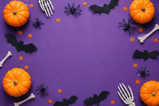 Halloween decorations on violet background. Flat lay pumpkins, bats, spiders, skeletons and confetti. Top view with copy space. Halloween concept.