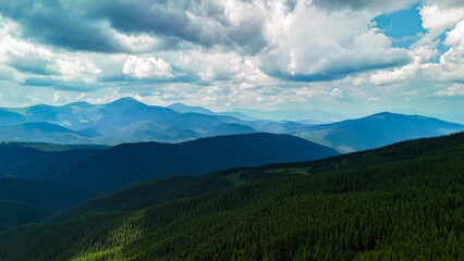 Obraz premium Moody layers of woodland ridges roll under a vast sky. Broken light glides across deep green canopies while distant summits blur to blue and a quiet wilderness feeling grows.