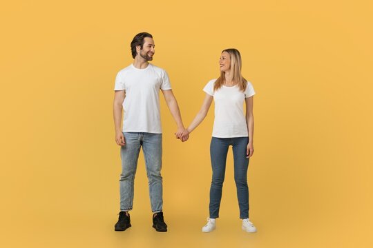 Happy Couple, Young Adult, Mixed Ethnicity, Smiling And Holding Hands Together In A Studio Setting With Bright Yellow Background. Joyful Moment Highlighting Connection And Affection. Concept