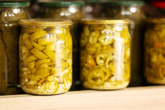 Home canned pickled sliced chili peppers in glass jars on shelf. Preserved hot jalapeno peppers for culinary recipes, food industry, and retail grocery market.