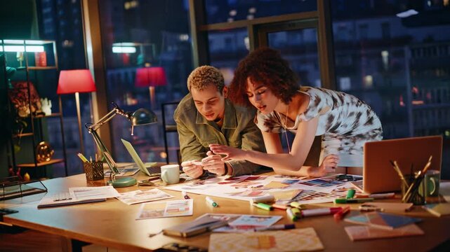 Creative couple reviewing color swatches in night studio. Designers brainstorm