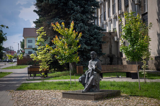 Kimry, Tver Region, Russia, 15 July 2026 &mdash; bronze statue of a seated cobbler in a small public park with benches and trees. the Monument to the Shoemaker