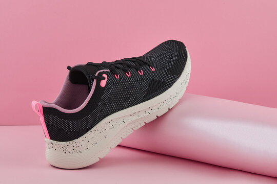 Black and pink athletic shoe with speckled sole, displayed against a pink backdrop, showcasing modern design and comfortable style