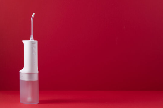 Compact electric oral irrigator standing upright on red backdrop, emphasizing modern dental health, hygiene and convenience