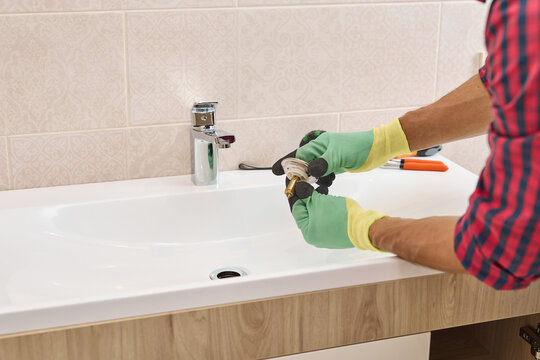 Plumber hands installing sink drain pop-up plug, repairing faucet and plumbing in a modern bathroom