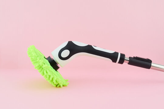 Electric spin scrubber with green microfiber head on pink background for modern home cleaning and hygiene