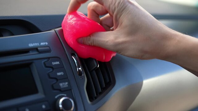 Man cleaning car air vent and dashboard with pink cleaning gel. Close-up of hand using sticky slime to remove dust from vehicle interior. Car detailing and maintenance concept.