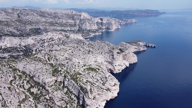 Cinematic aerial drone shot of the stunning white limestone cliffs of the Calanques dropping into deep dark blue Mediterranean water, beautiful coastal landscape in France