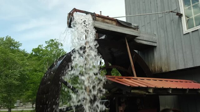 water wheel spins beside old barn and stream in mountain area during bright sunny day in summer season