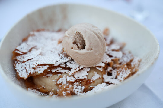 A creamy dessert topped with ice cream and crisp pastry flakes dusted with sugar in Greece, capturing Mediterranean sweetness and indulgent flavor.