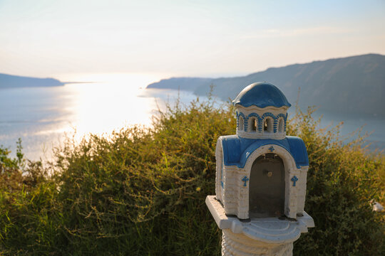A small blue‑domed roadside shrine overlooks the Aegean Sea at sunset in Greece, symbolizing faith and the serene beauty of Mediterranean tradition.