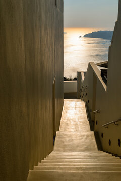A narrow stairway glows in golden light leading toward the Aegean Sea in Greece, capturing the quiet elegance of Mediterranean architecture.