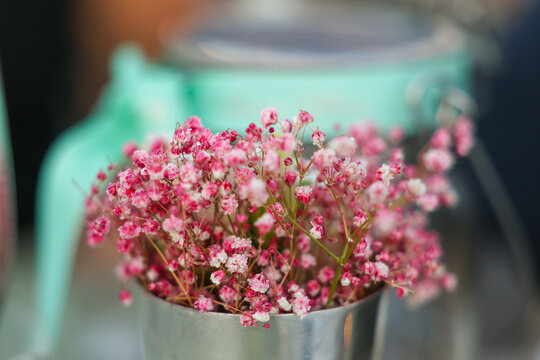 A small bouquet of pink flowers sits in a metal vase under warm sunlight in Greece, adding a touch of Mediterranean color and charm.