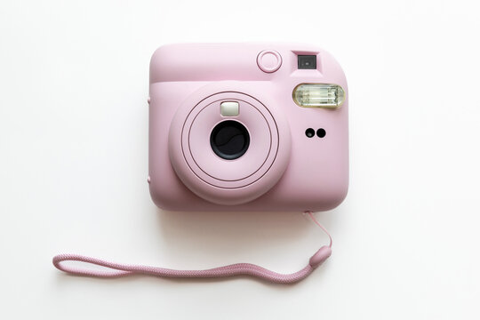 Pink instant camera featuring a round lens and a strap, placed on a clean white background, ideal for photography enthusiasts, capturing memories, and creative projects