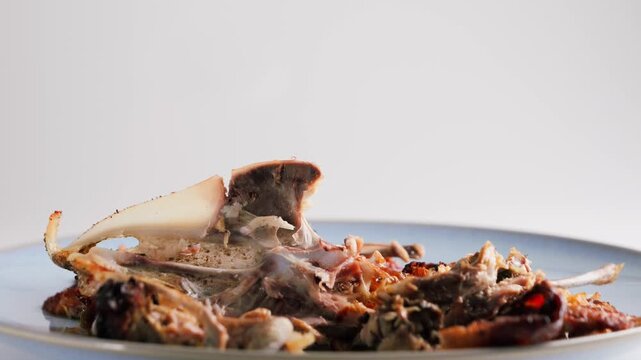 Food waste with leftover chicken bones on a plate. Kitchen leftovers and household food waste concept. High quality 4k footage