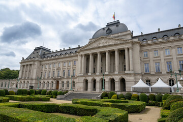 Obraz premium Grand neoclassical façade of the Royal Palace of Brussels surrounded by manicured gardens, presenting historic architecture and royal heritage beneath textured cloudy skies