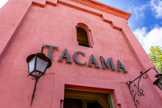 Ica, Peru, July 04, 2026: Pink stucco facade with TACAMA lettering, arched window, wrought iron details and decorative black lanterns beneath a bright blue cloudy sky.