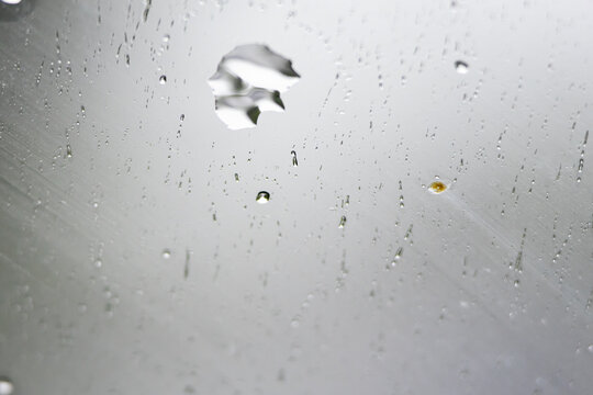 An irregular droplet silhouette floats among tiny beads on a pale reflective surface. Fine tracks of water hint at light wind and gravity creating a calm scientific feel.