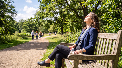 Fototapeta premium Woman relaxing on a park bench, enjoying the sunshine and fresh air.