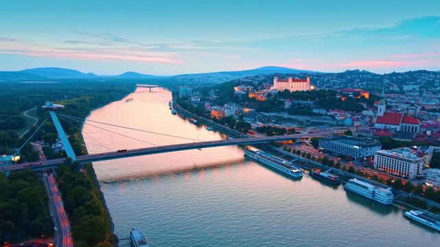 High angle view of Bratislava Castle and Most SNP. Sunset light colors the sky above the Danube River and historical city architecture.