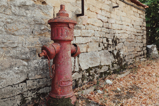 Weathered red fire hydrant beside an old stone wall in Burgundy, France, showcasing rustic village character, historic textures, and rural architecture.