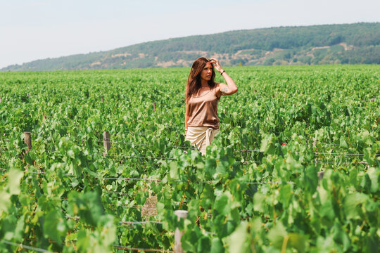Woman standing among vineyard rows in Puligny-Montrachet, Burgundy, France, surrounded by lush grapevines in one of the region's renowned wine-growing areas.