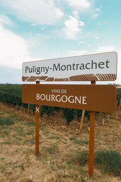 Roadside sign marking Puligny-Montrachet in Burgundy, France, surrounded by vineyard landscapes in the heart of a prestigious wine-producing region.