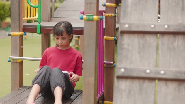 Asian kid enjoying a relaxing hobby, drawing digital art on tablet at outdoor school playground. Selective focus highlights creative elementary student spending personal leisure time with technology.