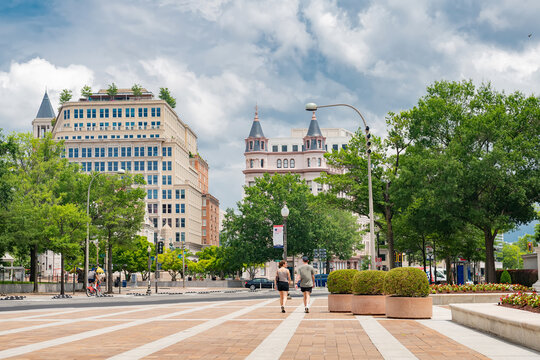 Pedestrians cross a landscaped downtown plaza beneath dramatic clouds in Washington DC.