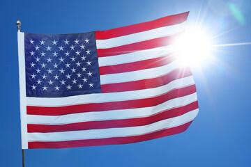 Obraz premium Flag of USA against bright sun in blue sky