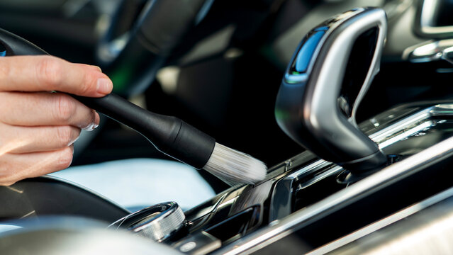 Hand cleans car's gear shift with soft brush