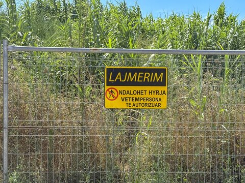Warning sign attached to wire fence beside overgrown vegetation