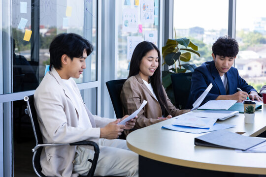 workers Group of young Asian business colleagues working together and reviewing reports during a project meeting in the meeting room at modern office.