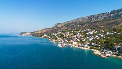 Fototapeta premium Aerial view of Mediterranean coastal town with red roof houses, rocky mountain, and blue Adriatic sea.