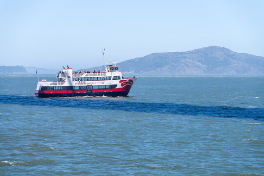 San Francisco, CA - July 15 2026: A red and white passenger ferry Royal Prince emerges from shadow of Golden Gate bridge in San Francisco bay