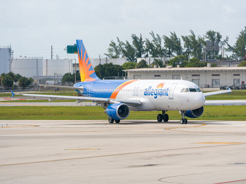 Allegiant Air passenger airplane drives on an airport runway asphalt past industrial tanks and trees before an aviation flight departure. USA, Fort Lauderdale, FL - May 18, 2026