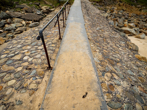 Pathway with metal grid and railing over rocky terrain. Sand and stones surround the walkway. No animals or plants visible in image
