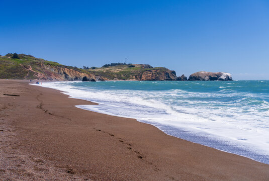 Waves crash along the unique dark pebble shoreline of Rodeo Beach located within the scenic landscape of the Marin Headlands in California.