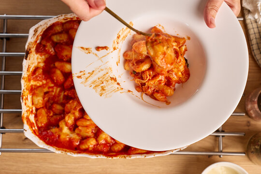 Gnocchi in tomato sauce with melted cheese placed onto white plate using serving spoon