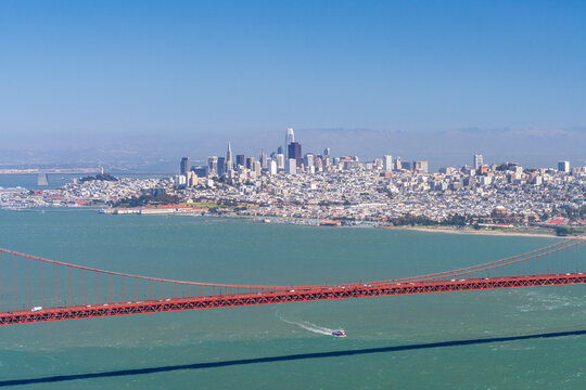 The Golden Gate Bridge spans the entrance of the bay with the San Francisco skyline visible from the rugged cliffs of the Marin Headlands.