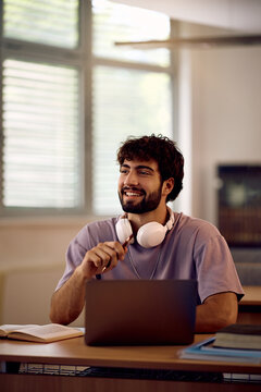 Happy male student using laptop while studying at university classroom.