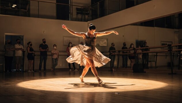 Medium shot of a dance academy open house spotlight on a lead dancer performing a fluid routine other performers and audience softly out of focus behind.