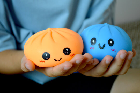 Hands gently holding two cute kawaii squishy dumpling character toys with happy smiling faces in orange and blue colors