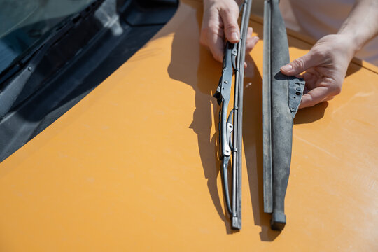 A woman replaces old windshield wipers with new ones on a car.