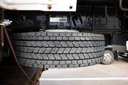 Spare tire truck wheel undercarriage black rubber vehicle maintenance garage closeup showing tread pattern, suspension frame, metal bracket, roadside repair, transport equipment