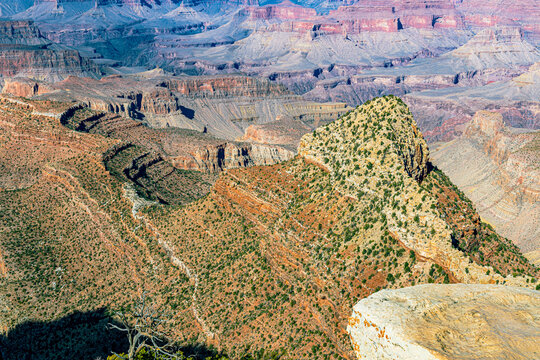 A juniper-covered butte juts into the hazy expanse of the Grand Canyon, revealing layered rock terraces, Arizona.
