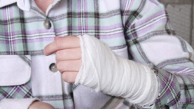 Woman with a white medical bandage on her hand and wrist. Injured hand of a person in a shirt, tightly wrapped with a gauze bandage. Medical bandage on the patient's hand after an injury or sprain