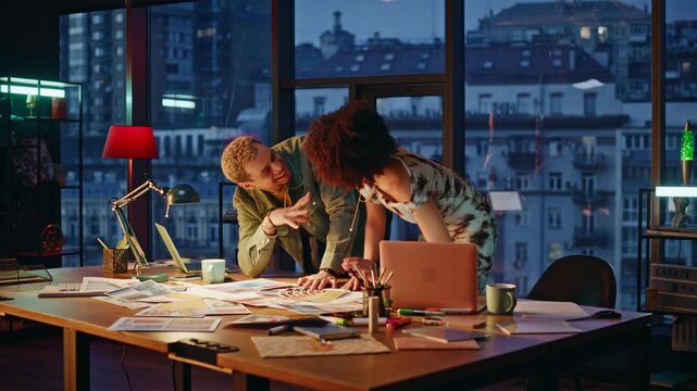 Two designers discussing color palette samples in evening office studio