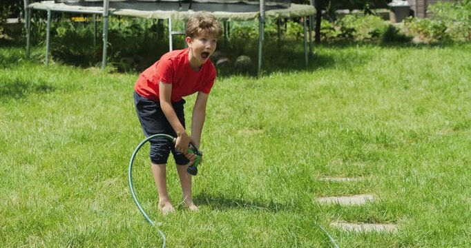 Funny barefoot little kid sprays water on his feet with a garden irrigation gun